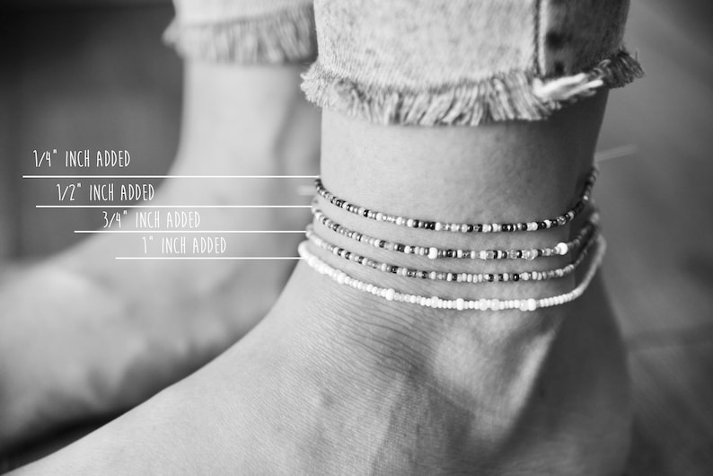 May include: Black and white image of an ankle adorned with four beaded anklets. The anklets vary in design, with beads in white, black, and silver. Text indicates measurements: 1/4 inch, 1/2 inch, 3/4 inch, and 1 inch added.