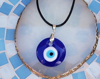 Pode incluir: Um colar com um pingente azul de olho turco em uma superfície de azulejos brancos e azuis.