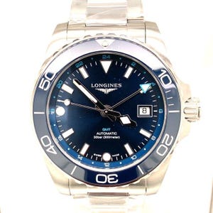 May include: A stainless steel Longines GMT automatic watch with a blue dial and bezel. The watch features luminous hands and markers, a date window, and is water-resistant to 300 meters. The watch has a silver band.