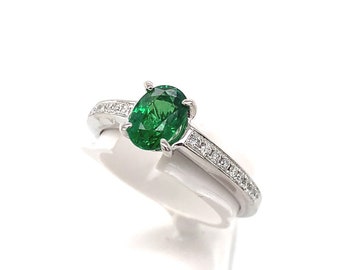 May include: A silver ring featuring a green oval gemstone set in a band of small diamonds.