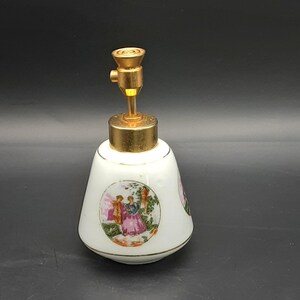 May include: White ceramic perfume bottle with a gold-colored metal top. The bottle features a painted scene of a couple in a garden. The bottle has a rounded base and a conical shape, with gold trim.