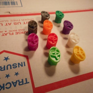 May include: Ten small, colorful, plastic, 3D printed wheels with a star-shaped design in the center. The wheels are in various colors, including green, red, orange, purple, white, and gray.