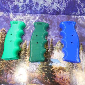 May include: Three 3D printed pistol grips in different colors: green, dark green, and blue. Each grip has a textured surface and two holes. The grips are labeled "RZO".