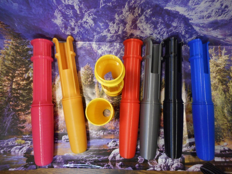 Op de afbeelding: Zes verschillende gekleurde plastic buizen met een gat in het midden. De buizen zijn rood, geel, grijs, zwart en blauw.