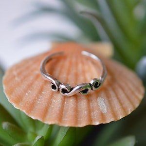 Puede incluir: Un anillo de dedo del pie de plata con un diseño delicado y en espiral. El anillo está apoyado en una concha.