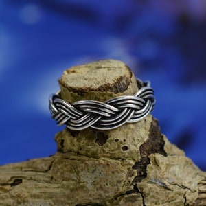 Puede incluir: Un anillo trenzado de plata sobre un trozo de madera desgastada sobre un fondo azul.