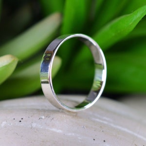 Peut inclure: Une bague simple en argent, avec une finition lisse et polie. La bague est présentée sur un fond gris clair.