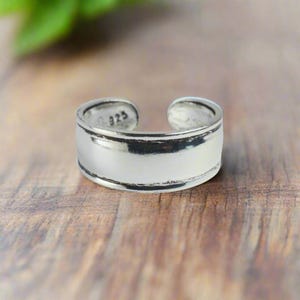 Könnte beinhalten: Ein silberner Zehenring mit einer glatten, flachen Oberfläche und einer leicht abgerundeten Kante. Der Ring ist innen mit der Nummer "925" gekennzeichnet.