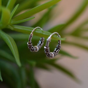 May include: A pair of silver hoop earrings with a decorative design. The earrings are small and delicate.