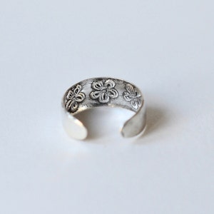 May include: Silver toe ring with a floral design. The ring is open and adjustable.