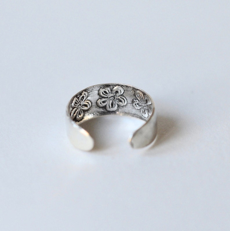 May include: Silver toe ring with a floral design. The ring is open and adjustable.