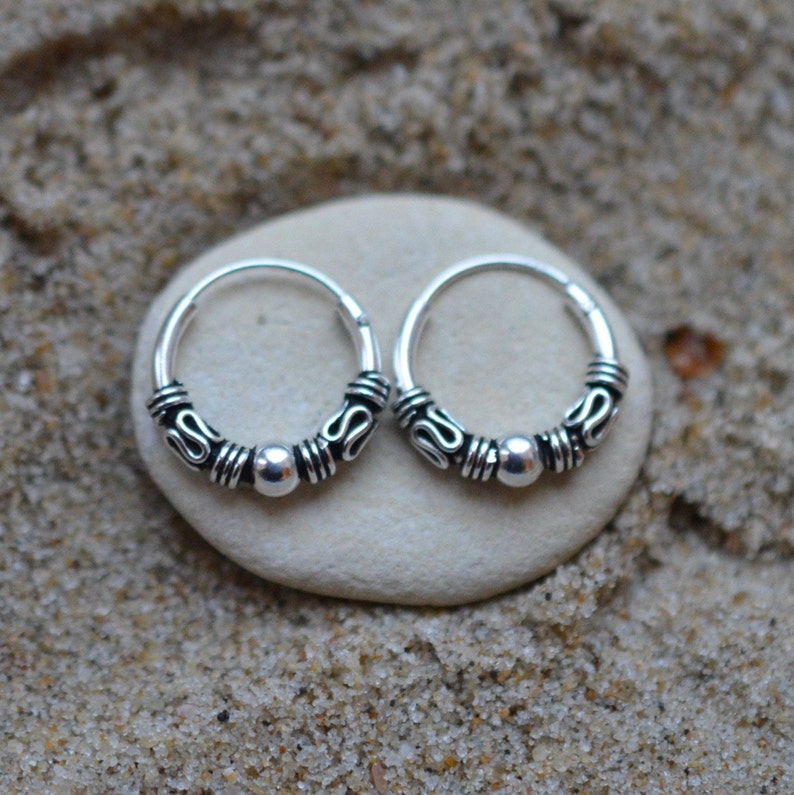 May include: A pair of small silver hoop earrings with a textured design and a small bead on each hoop.