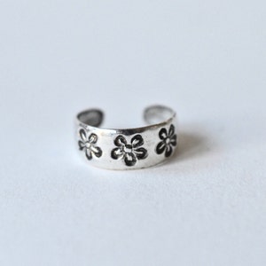 May include: Silver toe ring with three flower designs.