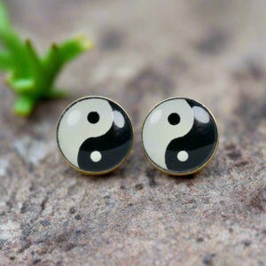 Könnte beinhalten: Ein Paar goldfarbene Ohrringe mit schwarzen und weißen Yin-Yang-Symbolen.