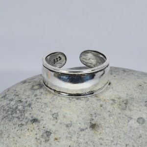 May include: A silver toe ring with a wide band and a smooth, polished finish. The ring is marked with the number "925" on the inside.