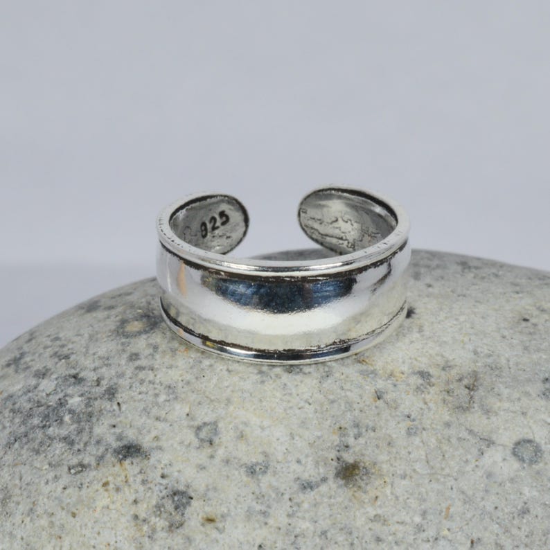 May include: A silver toe ring with a wide band and a smooth, polished finish. The ring is marked with the number "925" on the inside.