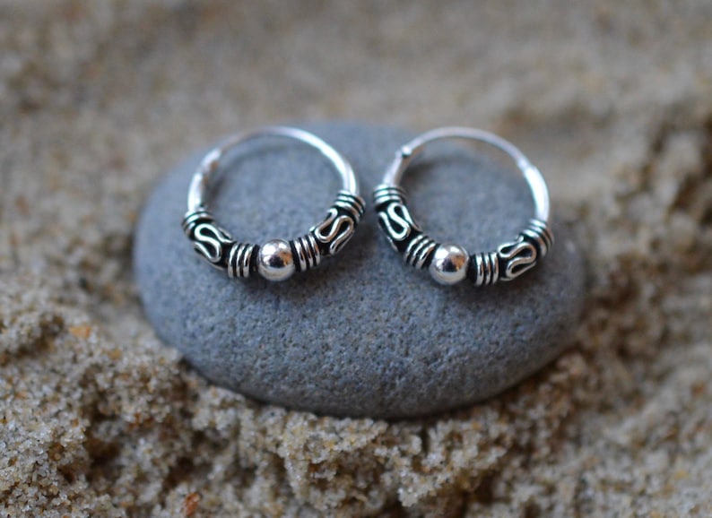 May include: A pair of silver hoop earrings with a beaded design. The earrings are small and delicate, and they would be perfect for everyday wear.