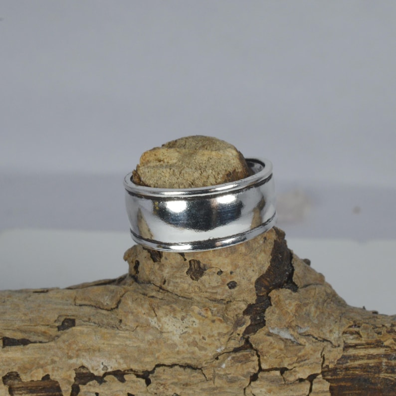 May include: A silver ring with a wide band and a smooth, polished finish.