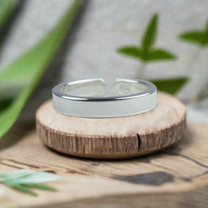 Könnte beinhalten: Ein silberner Zehenring mit einer glatten, flachen Oberfläche. Der Ring liegt auf einer Holzoberfläche.