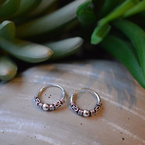 May include: A pair of silver hoop earrings with a small bead accent. The earrings are simple and elegant.