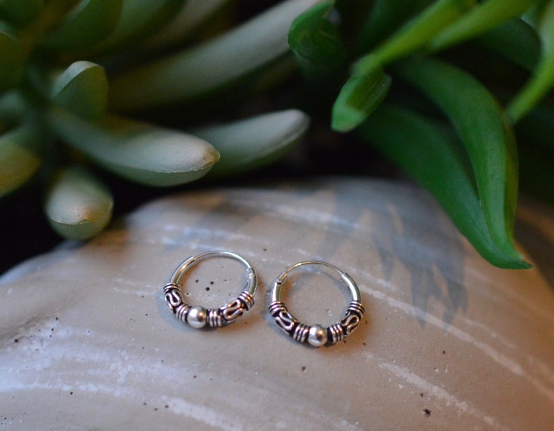 May include: A pair of silver hoop earrings with a small bead accent. The earrings are simple and elegant.
