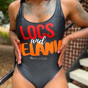 May include: Black one-piece swimsuit with the words "LOCS and MELANIN" in red, white, and orange. The swimsuit has a scoop neckline and a high-cut leg. The brand name "Thief's CULTURE" is printed at the bottom.