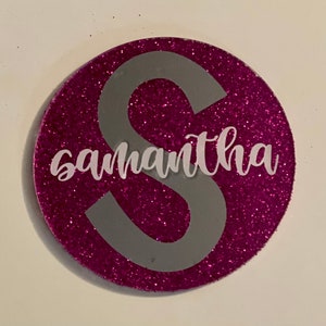 Könnte beinhalten: Ein pinkfarbener Glitzerkreis mit einem grauen Buchstaben S und dem Namen Samantha in weißer Kursivschrift.