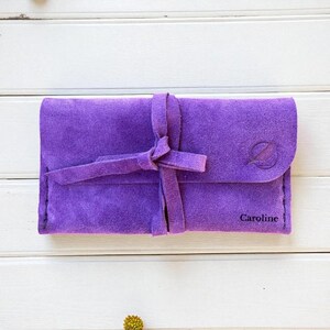 Handmade green suede leather wallet with soft texture and snap button closure, shown being held by hand. The wallet has a minimalist, long clutch design ideal for carrying cards, cash, or small essentials. Styled with a clean white wood background and green succulents, highlighting the natural and elegant feel of the product. A perfect choice for daily use or casual minimalist fashion lovers.