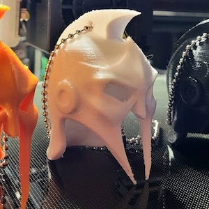 May include: Four 3D printed helmet keychains in orange, white, black, and red. Each keychain has a silver chain attached.