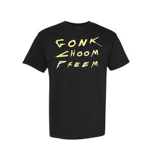 Può includere: T-shirt nera con la scritta gialla "GONK CHOOM FREEM". Il testo è scritto in stile manoscritto. La maglietta ha girocollo e maniche corte. Un capo casual.