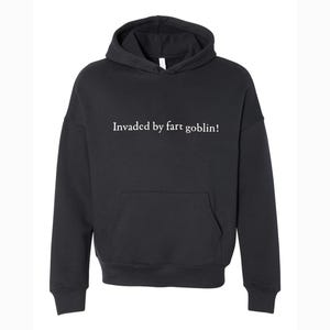 May include: Black hooded sweatshirt with a front pocket and drawstring. The text "Invaded by fart goblin!" is printed in white across the chest. The sweatshirt has a hood and long sleeves.