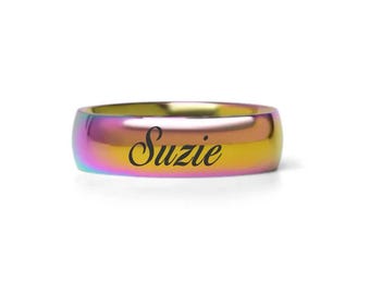 Puede incluir: Un anillo de metal con colores de arcoíris con el nombre "Suzie" grabado en letras negras.