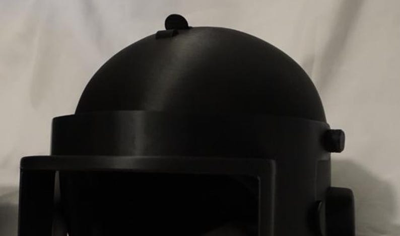 May include: A black helmet with a rounded top and a visor. The helmet has a small, round knob on the side.