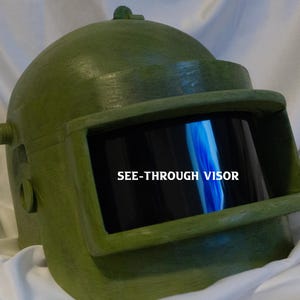 May include: A green helmet with a see-through visor. The visor has the text "SEE-THROUGH VISOR" printed on it.