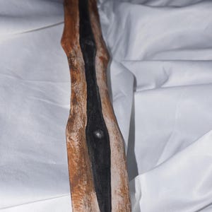 K&ouml;nnte beinhalten: Ein Holzschwert mit einer schwarz lackierten Klinge. Das Holz ist in einem braunen und wei&szlig;en Farbschema lackiert, was ihm ein verwittertes Aussehen verleiht.