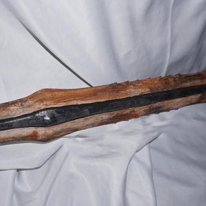 K&ouml;nnte beinhalten: Ein Holzschwert mit einer schwarzen Metallklinge. Das Schwert ist verwittert und hat eine raue Textur.