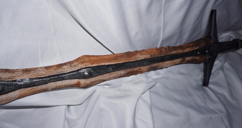 K&ouml;nnte beinhalten: Ein Holzschwert mit einer schwarzen Metallklinge. Das Schwert ist verwittert und hat eine raue Textur.