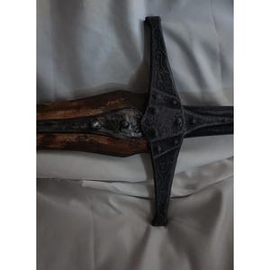 K&ouml;nnte beinhalten: Nahaufnahme eines schwarzen Schwertes aus Metall mit einem Holzgriff. Das Schwert hat komplizierte Details und eine spitze Spitze.