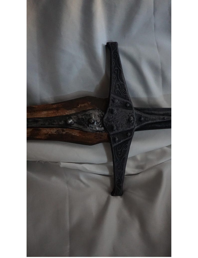 K&ouml;nnte beinhalten: Nahaufnahme eines schwarzen Schwertes aus Metall mit einem Holzgriff. Das Schwert hat komplizierte Details und eine spitze Spitze.