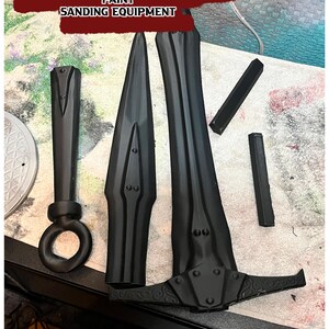 K&ouml;nnte beinhalten: Schwarze Plastikteile f&uuml;r ein DIY-Schwertprojekt. Die Teile umfassen die Klinge, den Griff und den Knauf. Der Text auf dem Bild lautet "DIY PARTS YOU WILL NEED: GLUE (SUPER GLUE IS GOOD ENOUGH) PAINT SANDING EQUIPMENT".