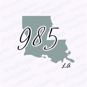 May include: A gray outline of the state of Louisiana with the number 985 written in black cursive script. The state abbreviation "La" is written in black cursive script below the outline.
