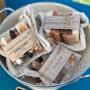 May include: A variety of colorful soap samples are displayed in a metal colander. Each bundle is wrapped in a crocheted net and tied with twine. The labels read "Brambly Woods Farm Variety Bundle Soap Samples Handmade in Frederick MD."