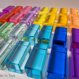 May include: A rainbow of colorful glass blocks arranged in rows. The blocks are translucent and have a smooth, polished finish. The blocks are arranged in a gradient from red to purple.