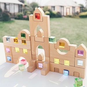 May include: A wooden castle building set with colorful translucent blocks. The blocks are made of clear plastic and have different colors, including red, yellow, green, blue, and purple. The blocks can be used to build a variety of structures, such as castles, towers, and houses.