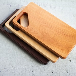 Puede incluir: Tres tablas de cortar de madera apiladas una encima de la otra. La tabla superior es de color marrón claro, la tabla del medio es de un tono de marrón más claro y la tabla inferior es de color marrón oscuro. Las tres tablas tienen un mango cortado en la parte superior.