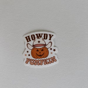 May include: A sticker featuring a cartoon pumpkin wearing a cowboy hat. The pumpkin is orange with a carved face. The text "HOWDY PUMPKIN" is written above and below the pumpkin in a brown, retro font. Small stars surround the pumpkin.