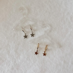 May include: Two pairs of hoop earrings with star-shaped charms. One pair is silver-toned and the other pair is gold-toned. Each earring features a small circular hoop with a dangling star pendant, displayed on clear plastic miniature hangers.