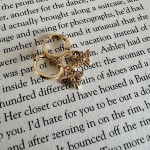 May include: Gold hoop earrings with a small bee charm. The bee charm has a gold body and black wings.