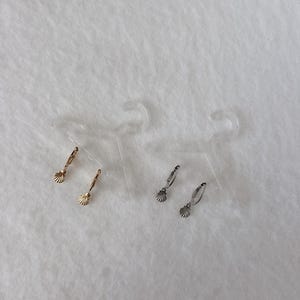 May include: Two pairs of hoop earrings, one gold-toned and one silver-toned, each featuring a small dangling seashell charm. The earrings are displayed on two clear plastic earring cards, each shaped like a miniature clothing hanger.