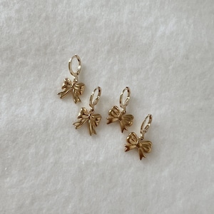 May include: Four gold hoop earrings with a bow charm hanging from each hoop.